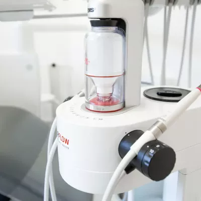 Nahaufnahme eines Airflow-Geräts zur professionellen Zahnreinigung. Im Hintergrund ist ein Behandlungsstuhl sichtbar.