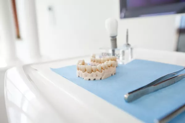 Nahaufnahme eines Implantatmodells mit Zahnersatz auf einem blauen Tuch. Daneben liegen zahnmedizinische Instrumente.